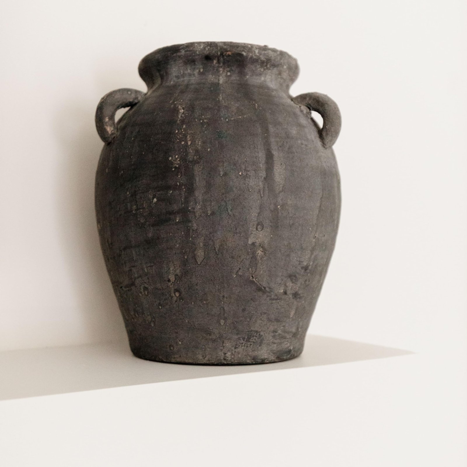 Dark gray, aged vase with two handles, sitting on a white surface
