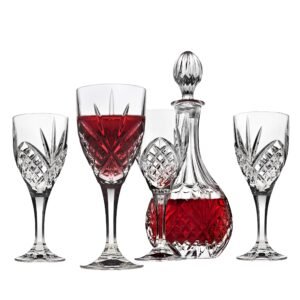 Crystal wine glasses and decanter filled with red liquid, on white background
